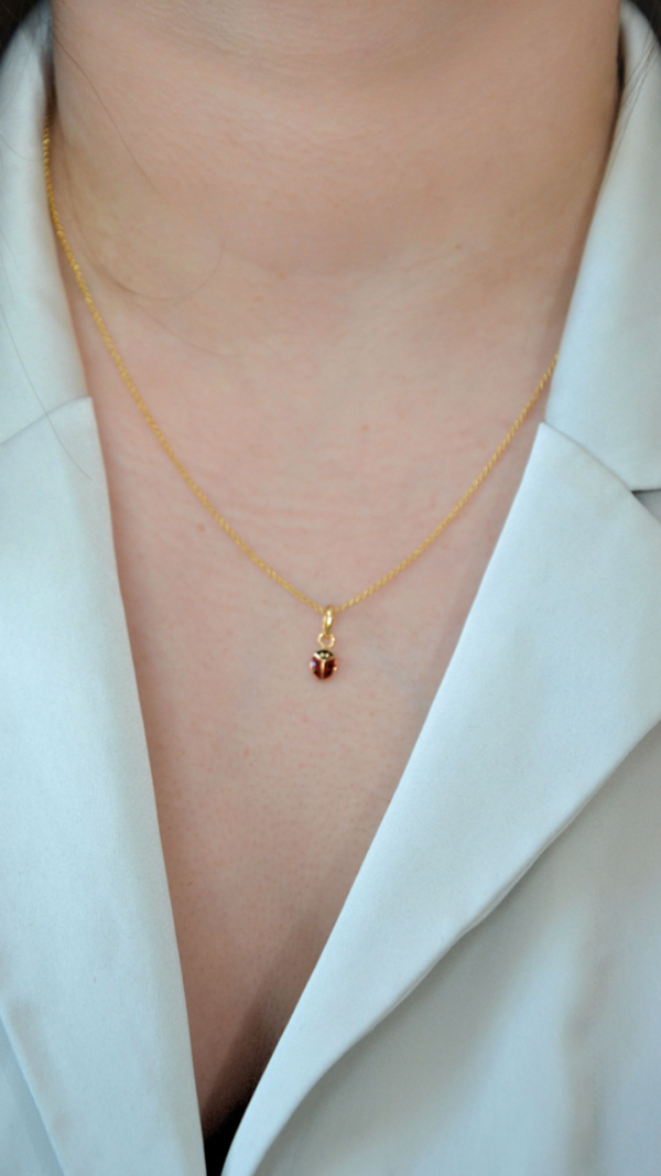 Collier plaqué or en forme de coccinelle rouge à pois noirs sur modèle